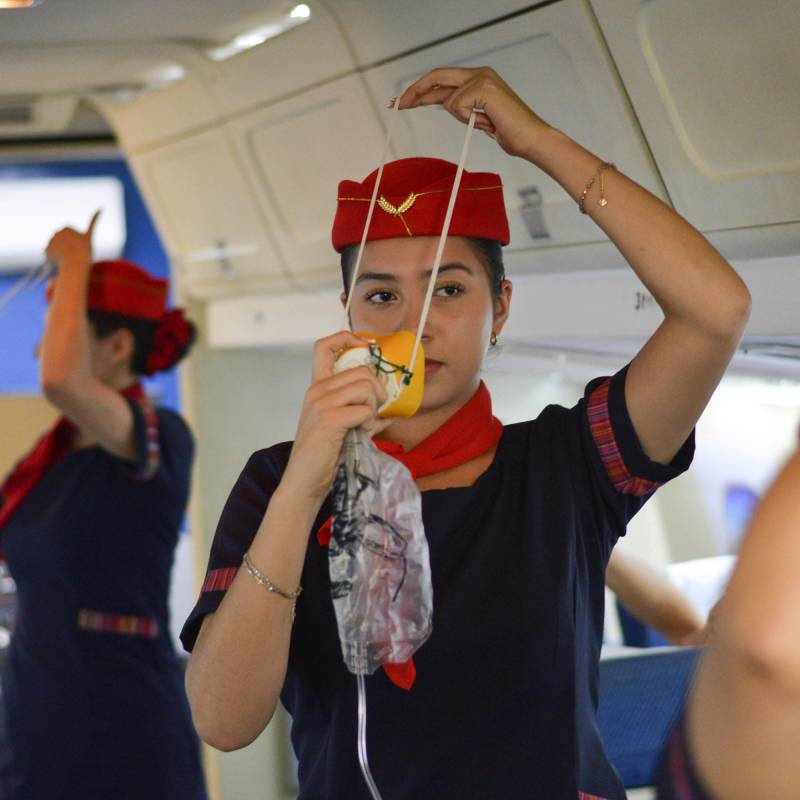 an air hostess demonstrating how to put on an oxygen mask