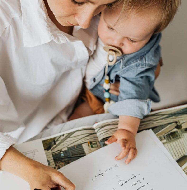 a woman holding a baby and looking at a book