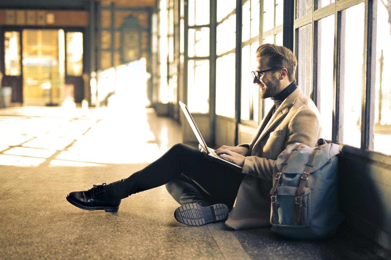 a man with a laptop sitting on the floor in a bright hallway