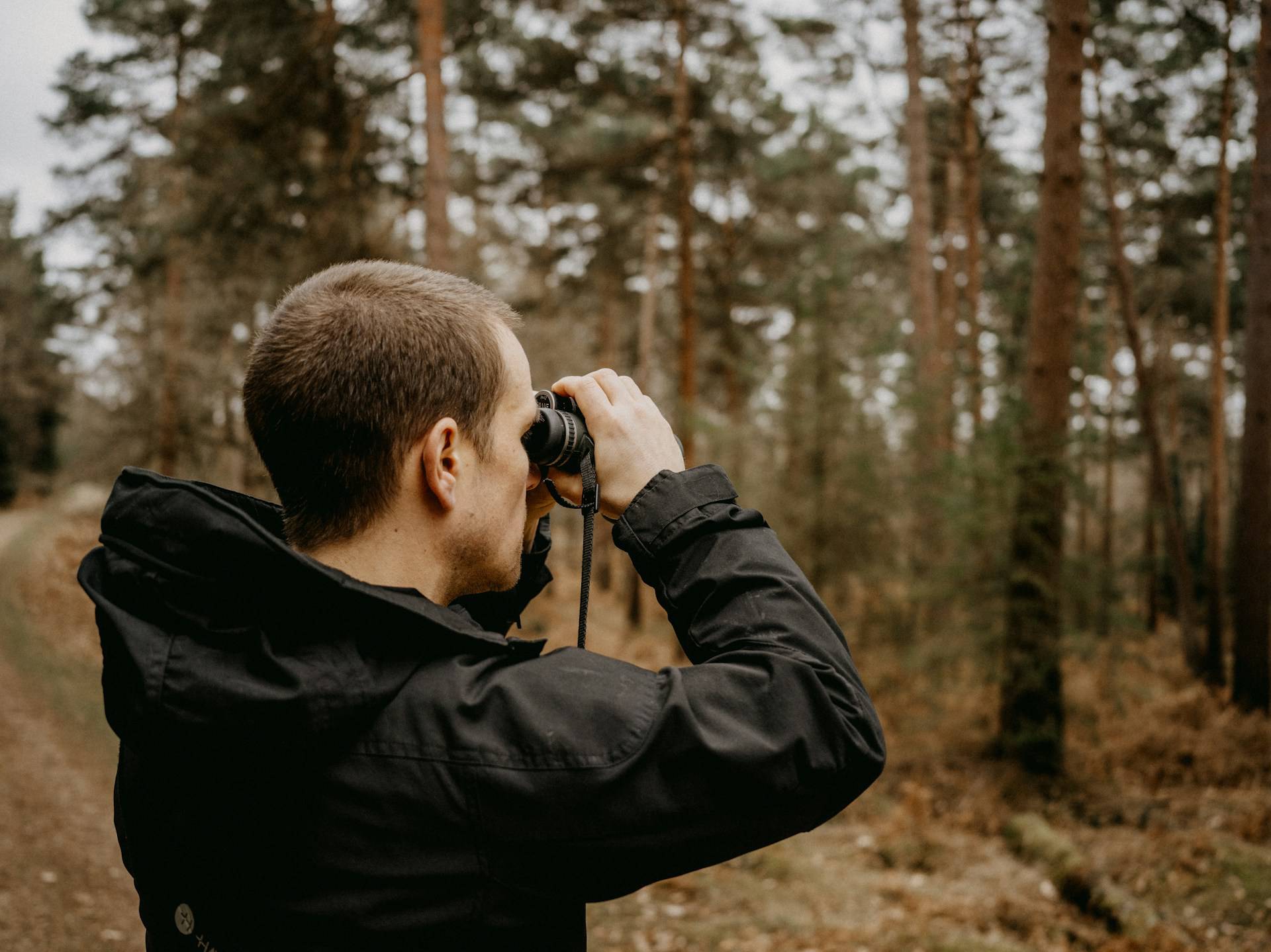 a man looking through binoculars in the woods