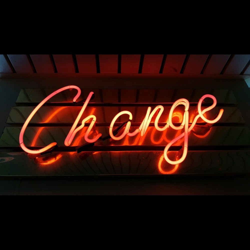 Neon “Change” sign glowing in orange-red light against a dark background.