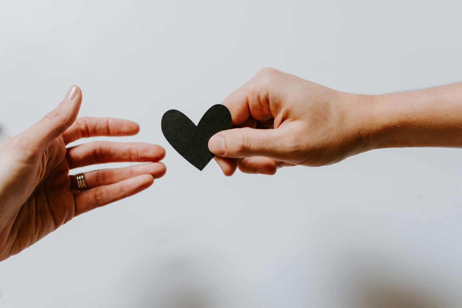 Hands exchanging a small black heart shape against a light background.