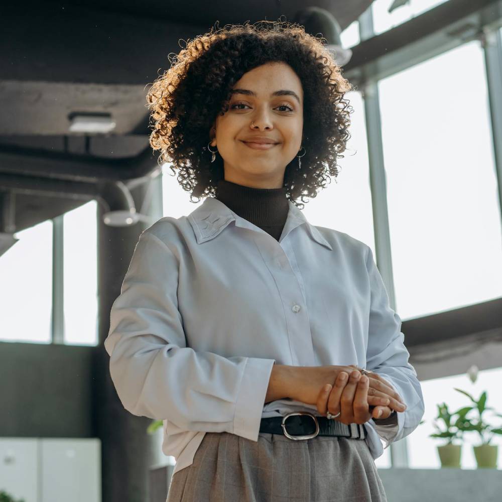 professional woman with curly hair standing confidently in a modern office space with natural light.