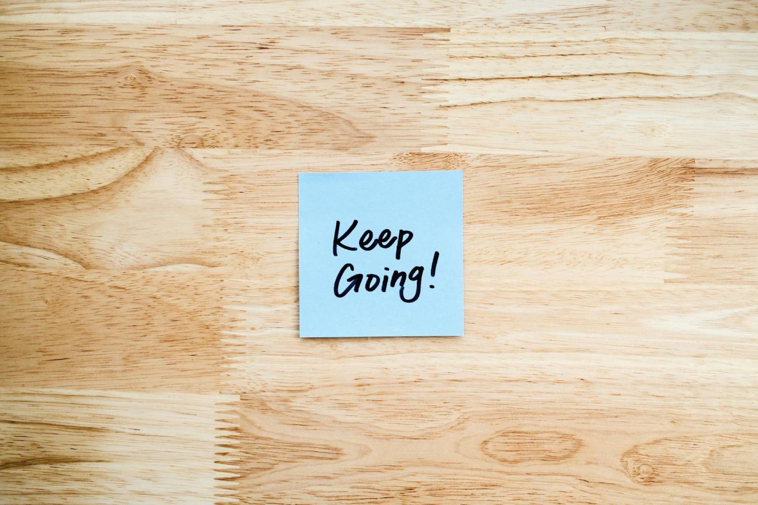 keep going written on a sticky note stuck to a wooden surface