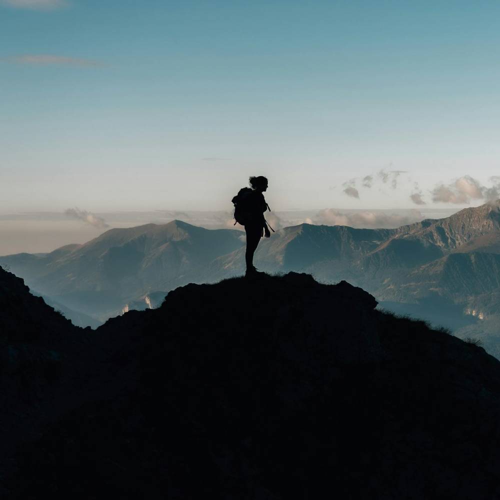 silhouette of a woman standing on top of a mountain