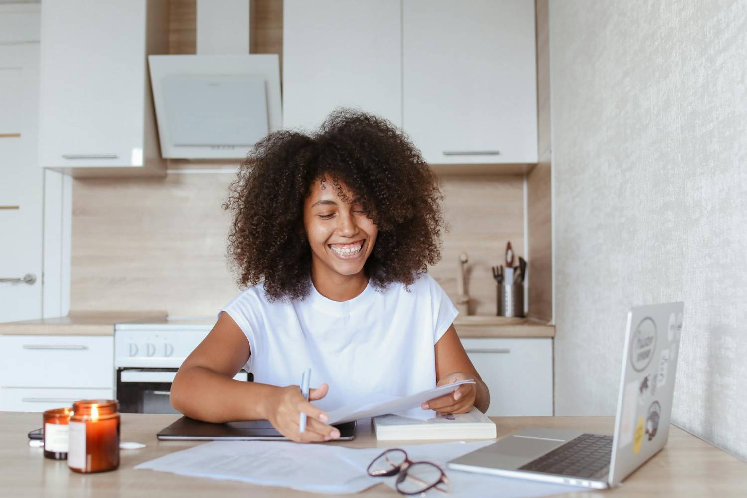 a smiling woman sitting in front of a laptop in a kithenette