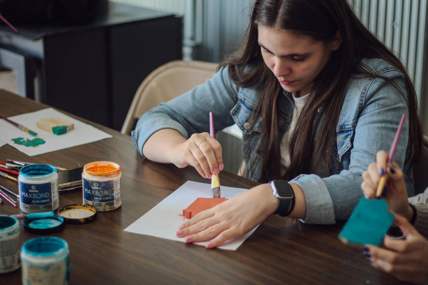 a woman painting an object resting on a sheet of paper