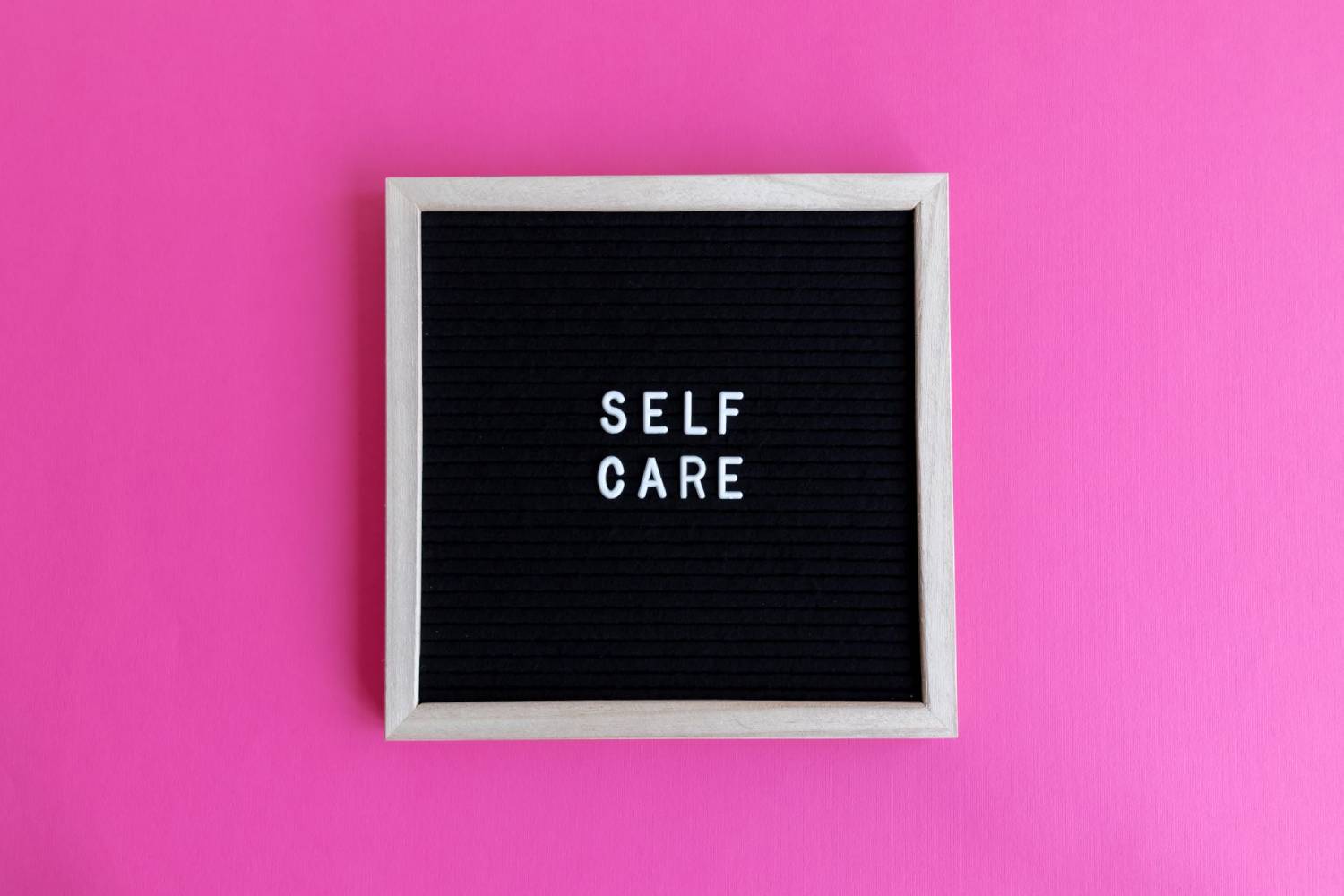 Letter board displaying the words “SELF CARE” against a bright pink background.