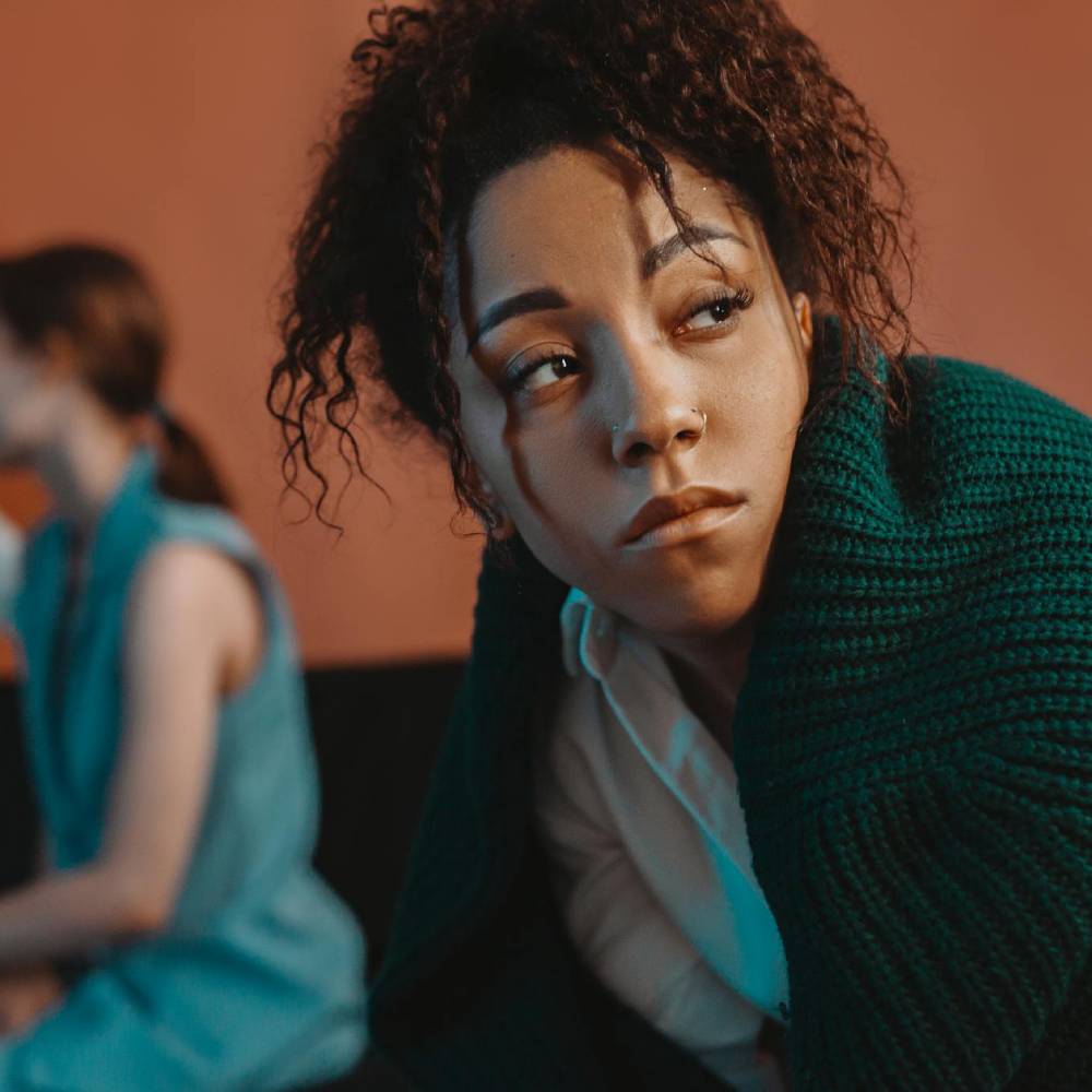 Person appearing withdrawn during a group counselling session while others speak in the background.