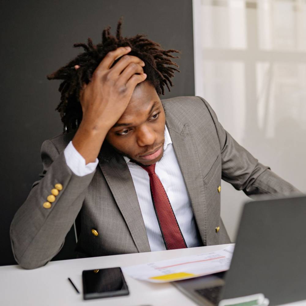 Stressed professional sitting at a desk with his hand on his head while looking at a laptop.