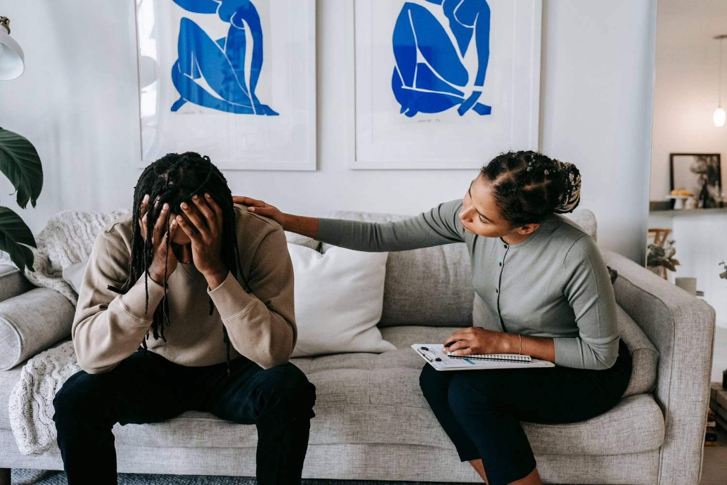 Therapist comforting a distressed person during a counselling session on a living room couch.