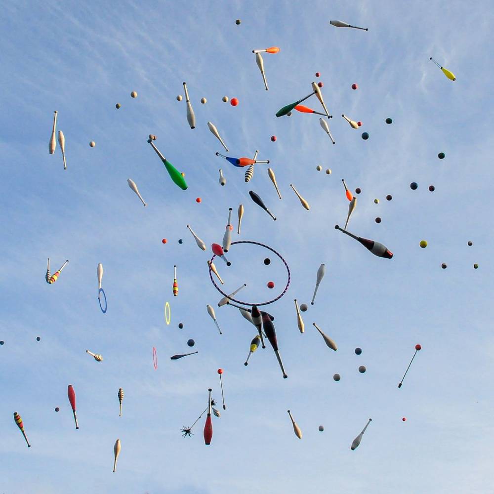 Vibrant juggling props in mid-air against a bright blue sky, showcasing motion and creativity.