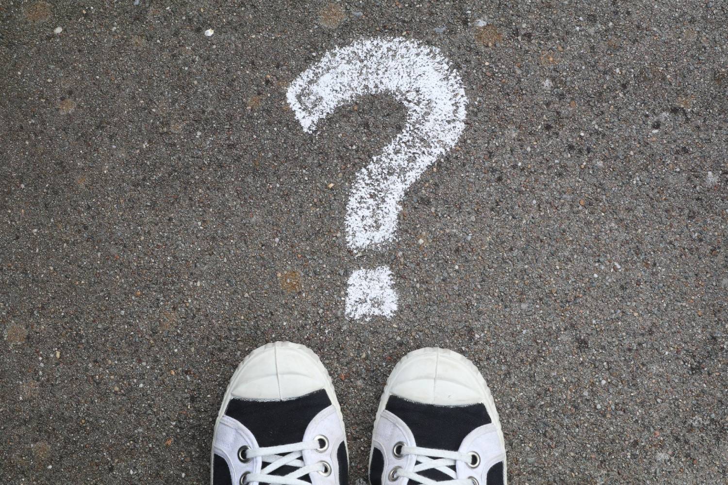 White question mark drawn on pavement in front of a pair of sneakers.