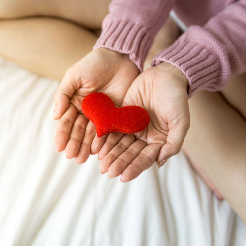 Hands gently holding a small red heart, symbolizing care, compassion and emotional support.