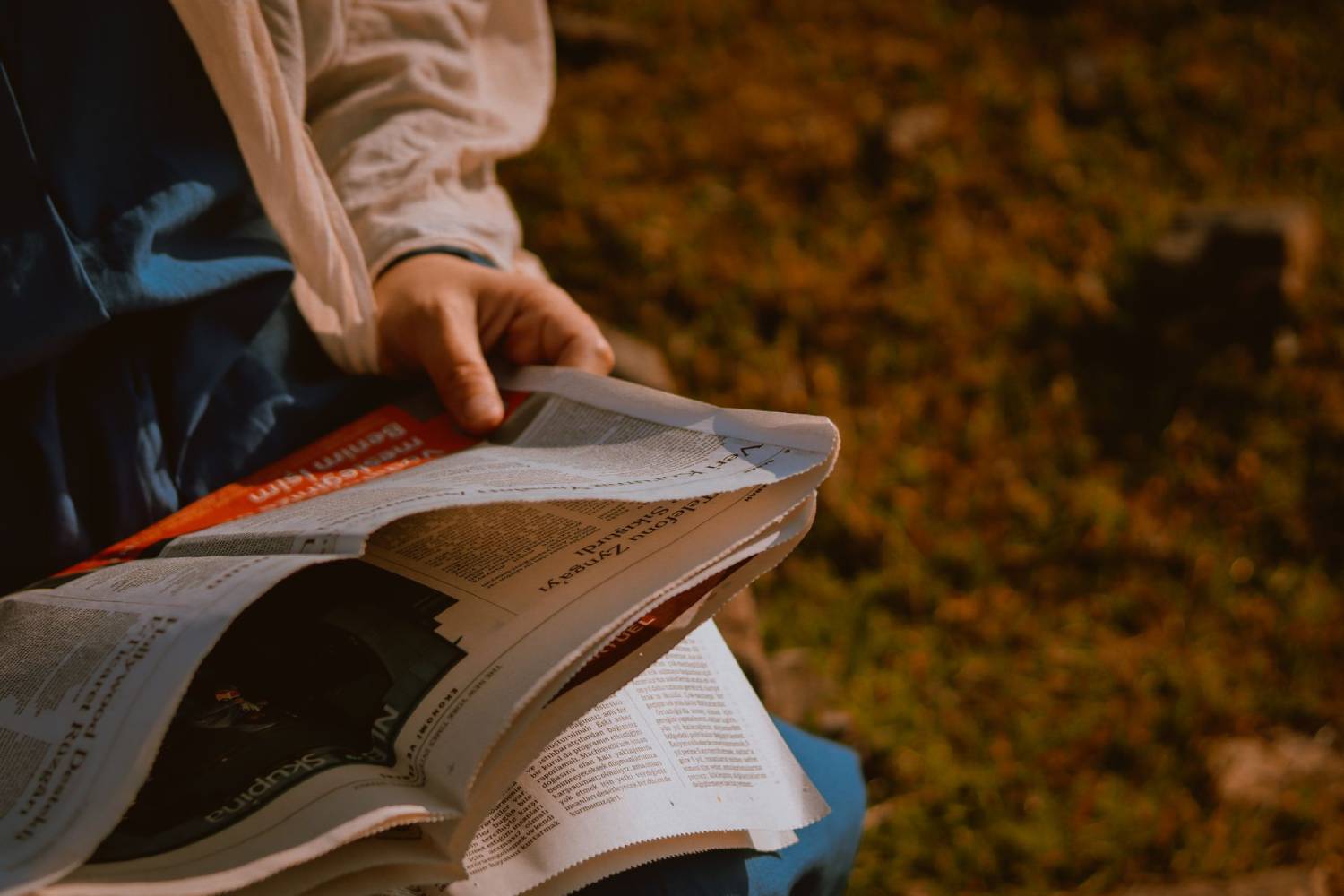 Person reading a newspaper outdoors in warm evening light.