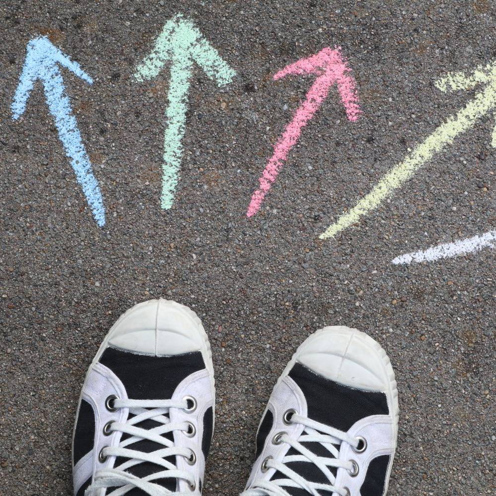 Black and white sneakers facing five colorful chalk arrows pointing in different directions.