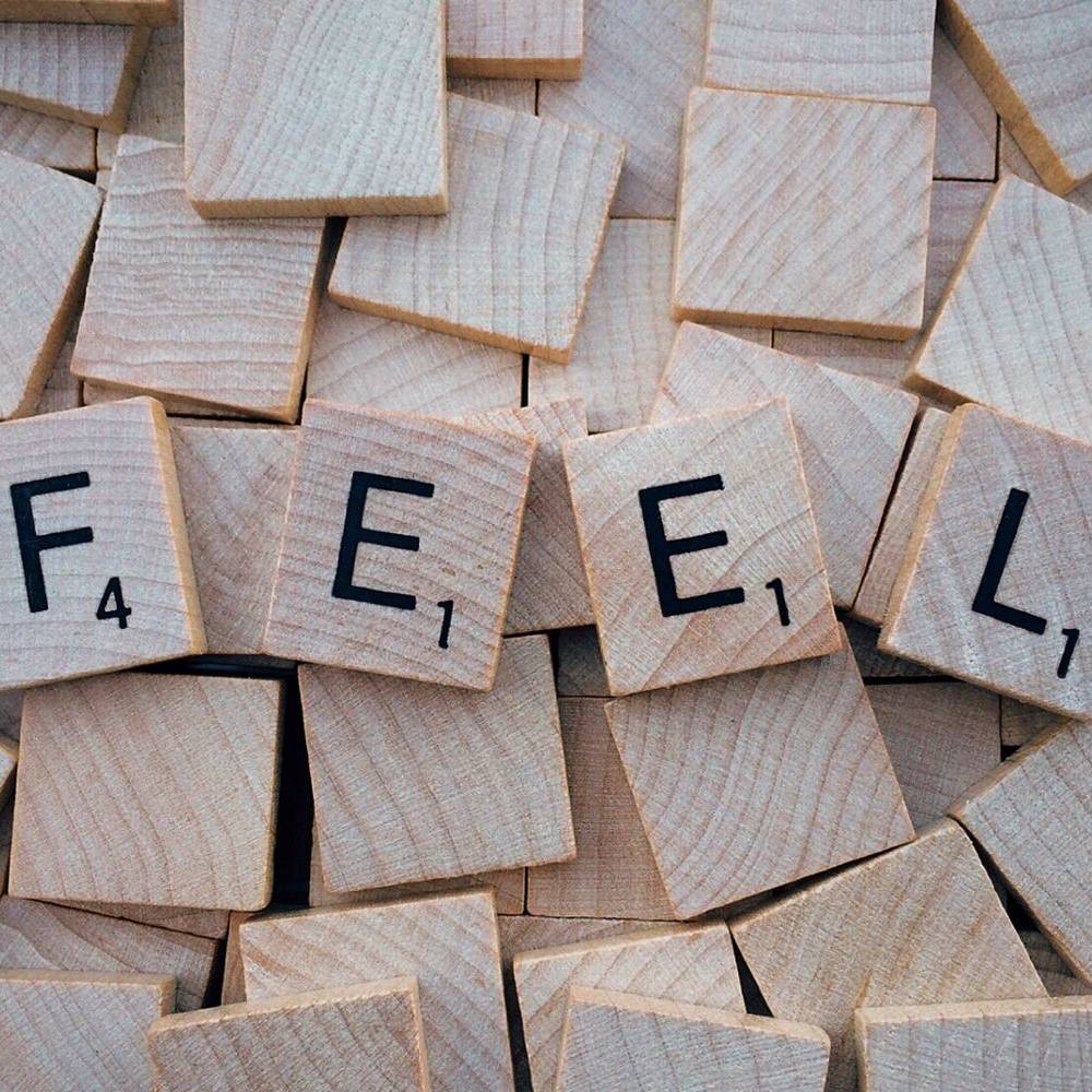 Wooden Scrabble tiles spelling “FEEL” arranged among blank tiles.